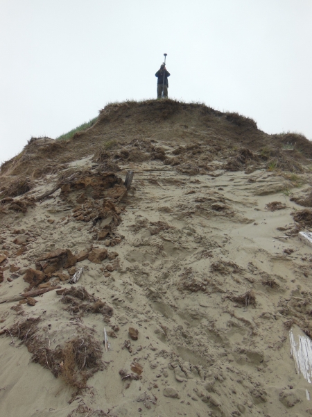 Figure 3. Mapping an eroding archaeological site. Note the wooden house posts  and other archaeological material exposed in the eroding bank. Photo courtesy of  Shelby Anderson 2013.